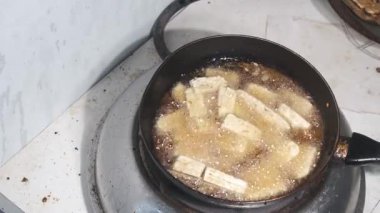 Tempeh, parlak gölgelerden derin gölgelere geçiş yapan bir tavada kızartılıyor. Altın dilimler cızırdayan yağda pişiyor ve ışıktaki kontrastlar dramatik bir hava yaratıyor. 4K