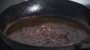 Çiğ fıstık bir tavada sıcak yağda pişiriliyor ve düzgün kızardığından emin olmak için eşit olarak karıştırılıyor. Kaynayan yağ ve yer fıstıklarının hareketleri otantik pişirme sürecini yakalar. 4K video görüntüleri