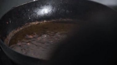 Kızarmış fıstıklar tavadaki kızgın yağdan kaldırılıyor, altın ve çıtır çıtır çıkarlarken buharlaşıp parlıyorlar. Aksiyon yemek pişirmenin, dokunun ve ısının son aşamasını yakalar. 4K görüntü.