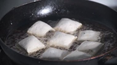 Beyaz tofu, siyah bir tavada kızgın yağda kızartılıyor. Altın rengine dönüşmeye başladığında cızırdıyor. Soluk soya peyniri ve koyu tenli tava arasındaki zıtlık dokuyu ve ısıyı ön plana çıkarıyor. 4K görüntü videosu