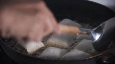 Tofu parçaları tavanın içinde kaynayan kızgın yağda kaynatılıyor. Cızırdayan ses ve dalgalanan yağ tofunun altın rengine eşit derecede pişerken sıcaklığın yoğunluğunu gösteriyor. 4K görüntü videosu.