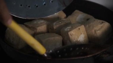 Kızarmış altın tofu tavada kaynayan sıcak yağdan kaldırılıyor, çıkartılırken parlıyor ve buhar çıkıyor. Kıtır kıtır dokular ve zengin renkler mükemmel piştiğini gösteriyor. Bu canlı anı yakalıyor. 4K