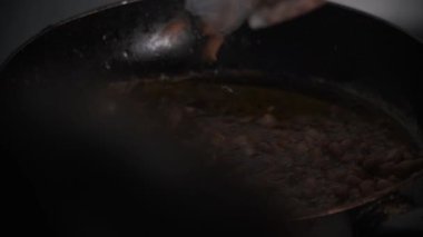 Çiğ fıstık sıcak yağla dolu siyah bir tavaya yerleştiriliyor. Cızırtılı süreç, geleneksel yemek pişirme yöntemlerini ön plana çıkaran kızartma çalışmalarının başlangıcını yakalıyor. Bu sahne yemek için ideal. 4K