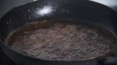 Fıstıkları kızartırken siyah bir tavada sıcak yağ kabarcıkları otantik bir yemek sahnesi yaratıyor. Cızırdayan köpük ve altın doku geleneksel gıda hazırlığını temsil eden kızartma sürecini vurguluyor. 