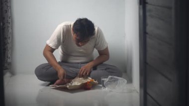 Eski püskü giysiler içinde Asyalı bir adam ona verilen pirinci yiyor, karnını doyurma işine odaklanıyor. Sahne, şükran, hayatta kalma ve günlük yiyecek mücadelesini yansıtıyor. İzole edilmiş arkaplan.