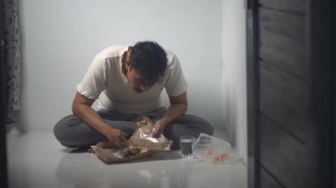 Evsiz bir adam yerde otururken hevesle yemek yiyor. Görüntüler bir açlık ve hayatta kalma anını yakalıyor, gerçek yaşam sosyal koşullarını yansıtıyor. Yoksullukla ilgili stok görüntüleri için uygun