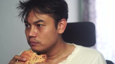 Eski püskü beyaz elbiseli Asyalı bir adam iştah ve açlığın ifadesini yakalamak için hevesle ekmek yiyor. Sahne basitliği, mütevazı yaşam tarzını ve günlük insan rutinlerini yansıtıyor. Uygun. 4K