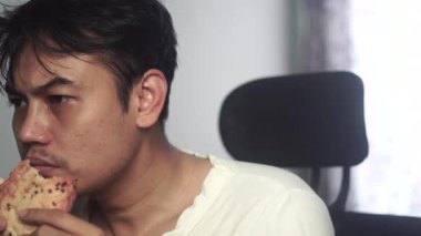 Beyaz gömlek giyen evsiz bir adam oturuyor ve bir parça ekmek yiyor, gözlerini tam karşıya odaklıyor. Görüntüler günlük mücadele ve hayatta kalma sahnesinin gerçekçi bir anını yakalıyor. 4K görüntü