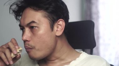 Bir adam sakince bir parça ekmek çiğnerken dikkatle izliyor. Görüntüler günlük hayatın rahat ve doğal bir anını gösteriyor, günlük yeme davranışlarına ve konsantrasyonuna odaklanıyor. 4K görüntüsü