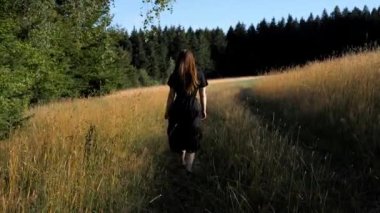 Siyah elbiseli genç bir kadının sabah vakti ormanın dışındaki bir tarlada yürürken görüntüsü..
