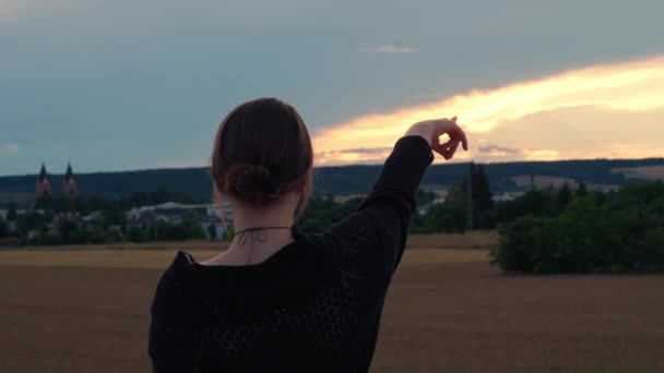 黒い服を着た少女が日没に空を指差した カメラを被写体に戻す — ストック動画