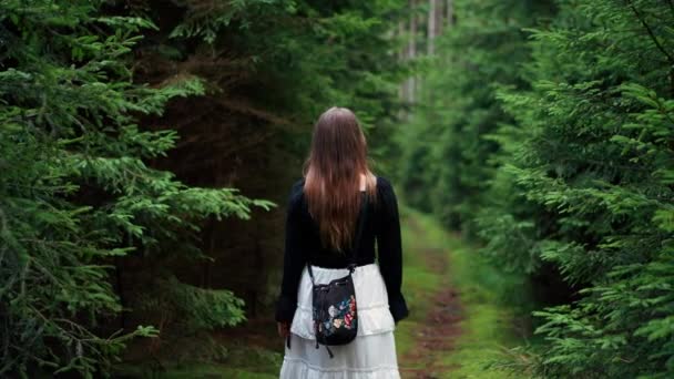 長い髪の少女は 日中に混雑した森の道を歩いています 自然の中でリラックスしたり歩いたり 新しい場所や経験を発見するのに理想的な夏の天気 — ストック動画