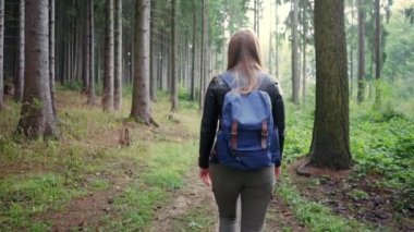 Genç kız sonbahar ormanı yolunda tek başına seyahat ediyor. Bedava güzel günlerin tadını çıkarmaya çalışan kadın sırt çantasının yavaş çekimleri.