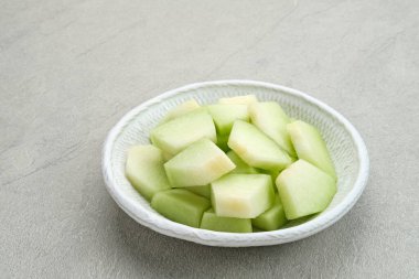 Gri arka planda küçük tabakta servis edilen kavun dilimleri.. 