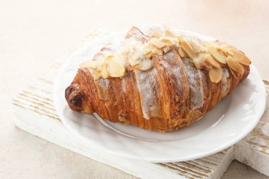 Beyaz tabağa şeker serpiştirilmiş badem kruvasanı. 