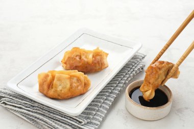 Gyoza, sulu tavuk ve lahana ile yağda kızartılmış hamur tatlısı. Soya soslu beyaz tabakta servis edilir.