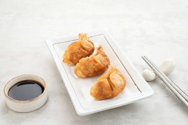 Gyoza, sulu tavuk ve lahana ile yağda kızartılmış hamur tatlısı. Soya soslu beyaz tabakta servis edilir.