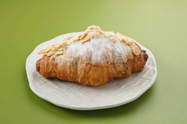 Beyaz tabağa şeker serpiştirilmiş badem kruvasanı. 