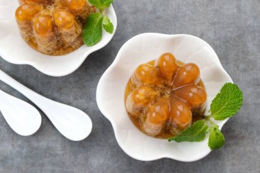 Puding Lumut Gula Merah, yosun desenli, tatlı ve kremalı, nane yaprağıyla servis edilen küçük beyaz tabakta.