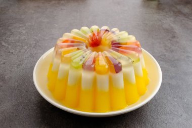 Meyve soslu lezzetli mango sütlü puding. Beyaz tabakta servis edilir.