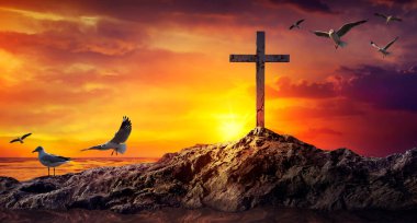 Silhouetted christian cross standing on a rock in the sea or ocean  clipart