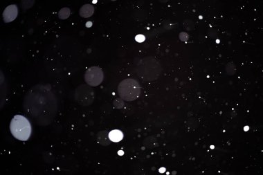 Koyu bir zemin üzerinde uçan karın arka planı, yumuşak odaklı kar dokusu.