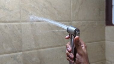 Bir insan banyodaki duş spreyine bastırarak duvara su sıkarak suyu boşa harcıyor.