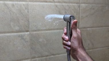 Bir insan banyodaki duş spreyine bastırarak duvara su sıkarak suyu boşa harcıyor.