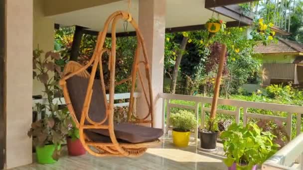 縁側に植物や緑の庭に囲まれた風に揺れる木の椅子のスイング — ストック動画