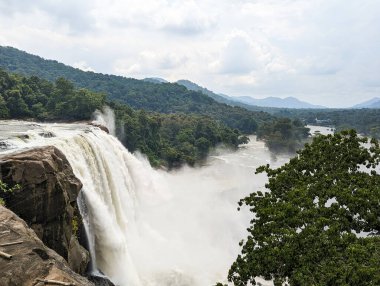a mystical white waterfall at the center of a dark green forest surrounded by hills and mountains in the summer