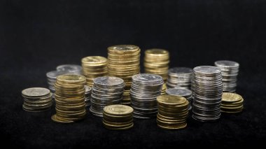 Yakın plan çekimde altın ve gümüş sikkeler siyah arka planda izole edilmiş farklı boyutlardaki kulelerde dizilmiş ve istiflenmiştir.