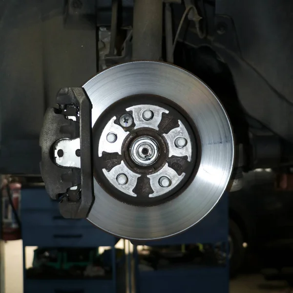 closeup of an automobile brake rotor disc with a hydraulic caliper under maintenance in an auto service center