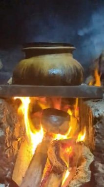 Çamur ve taştan yapılmış bir odun ocağında, karanlık bir yerde dumanla yanan eski, geleneksel bir tencere.