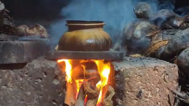 暗い場所で煙で燃える泥と石で作られた薪ストーブの熱の下で古い伝統的な調理鍋 — ストック動画