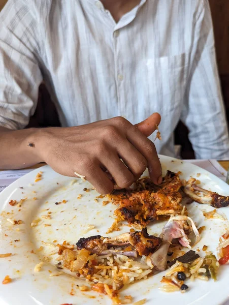closeup of a dirty food plate with leftovers of chicken bones and biriyani rice with masala eaten by a man in a restaurant