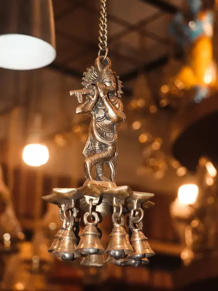 a wind chime bell with lord krishna playing flute bronze figure hanging on a chain in a gift store in the market for souvenir items