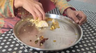 Kadın kahvaltıda idli 'sini sambar körisiyle karıştırarak yiyor. Masadaki çelik tabaktaki elini kullanarak.