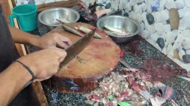 Balık satıcısının elleri, balık pazarında içi atık ve kanla dolu bir masada bıçakla taze çiğ balığı parçalara ayırıyor.