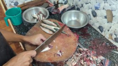 Balık satıcısının elleri, balık pazarında içi atık ve kanla dolu bir masada bıçakla taze çiğ balığı parçalara ayırıyor.
