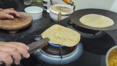 Kadının eli, fırının üzerinde ustaca bir beceriyle gaz alevi üzerinde phulka roti pişiriyor. Bu da onu şişirip mutfaktaki tüylü, lezzetli bir ekmek haline getiriyor.