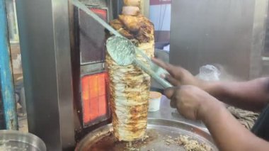 Bir sokak restoranının mutfağında, yetenekli bir işçi ızgara tezgahında dönen et kulesinden ince dilimlenmiş ve kıyma doğranmış baharatlı shawarma yapar.