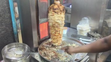 Bir sokak restoranının mutfağında, yetenekli bir işçi ızgara tezgahında dönen et kulesinden ince dilimlenmiş ve kıyma doğranmış baharatlı shawarma yapar.