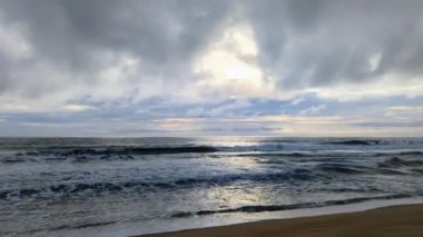 Muson mevsiminde gökyüzünde kara bulutlar olan bir kumsalda deniz gelgitleri