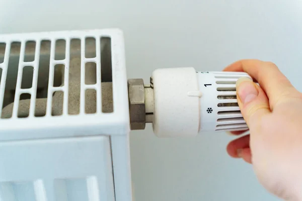 stock image A womans hand switches the radiator heating regulator to a minimum to save heat energy due to rising prices for nuts and utilities.