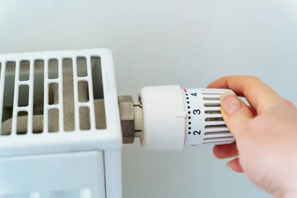 A hand turns the regulator on the heating radiator of the house. The concept of saving resources and heat energy in connection with the energy crisis.