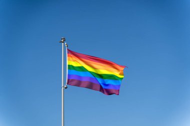 LGBTQ gökkuşağı bayrağı açık mavi gökyüzüne doğru dalgalanıyor.