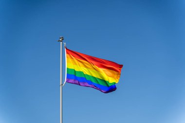 LGBTQ topluluğunun gökkuşağı bayrağı açık mavi gökyüzünün zemininde dalgalanıyor