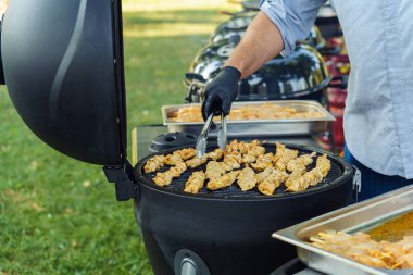 Barbekü partisi sırasında bahçede tavuk ızgara yapan bir adam..