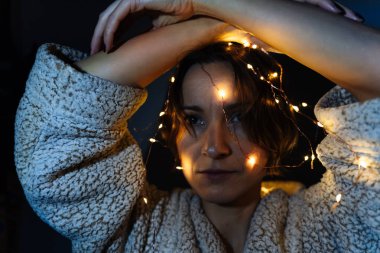 Bir kadın ellerini başının üstünde tutan parlak bir Noel çelengiyle süslenir..