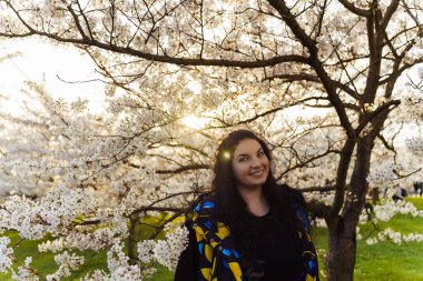 Genç, çekici, uzun siyah saçlı bir kadın parkta çiçek açan kiraz bahçesinde vakit geçirmekten zevk alıyor..